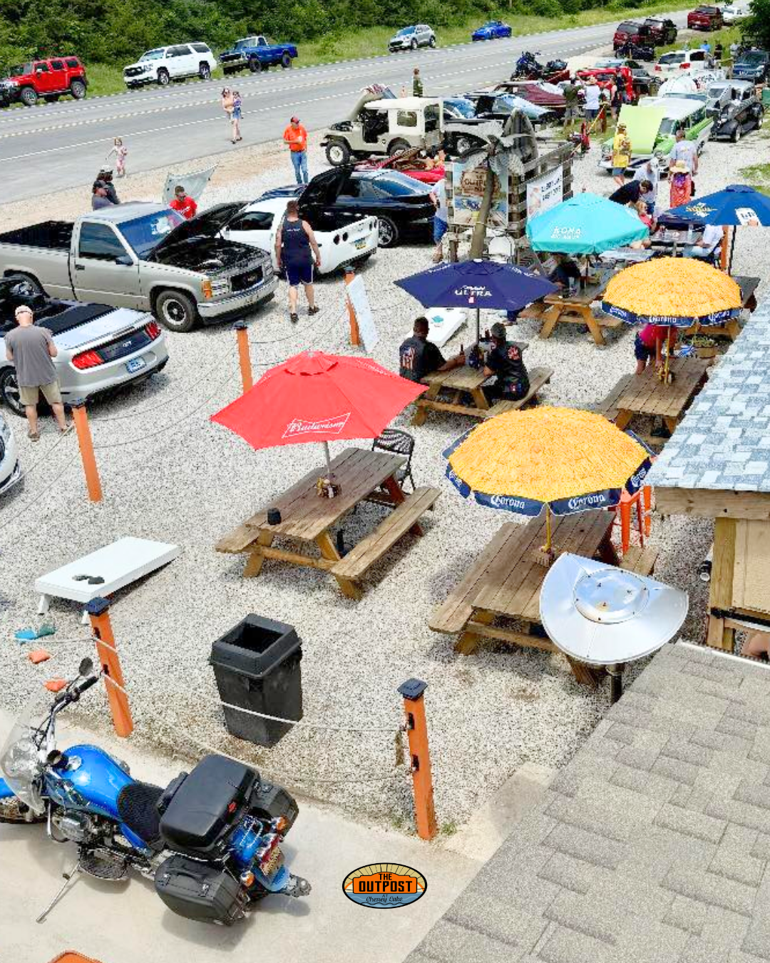 Car and bike show in The Outpost parking lot with classic vehicles and people relaxing at picnic tables